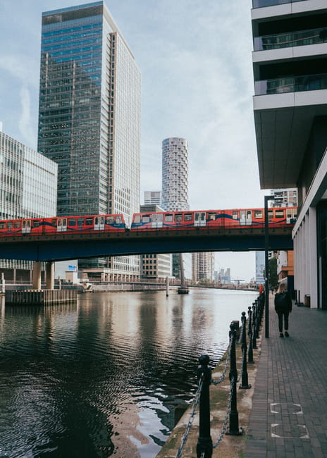 Aerial view of the Canary Wharf financial district showing numerous modern high-rise office buildings and residential towers, including a distinctive twisting skyscraper, situated along a waterway wit